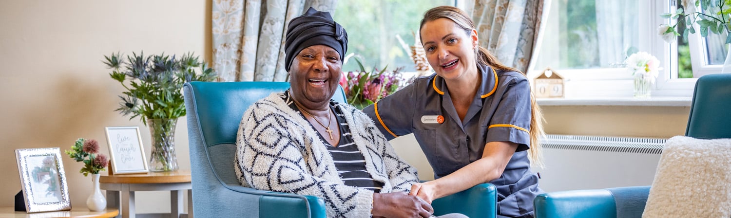 HC One care home resident sitting with carer on green chairs